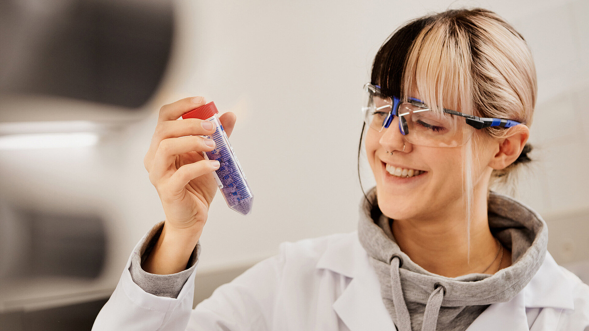 Young scientist in safety glasses examining test tube with purple solution