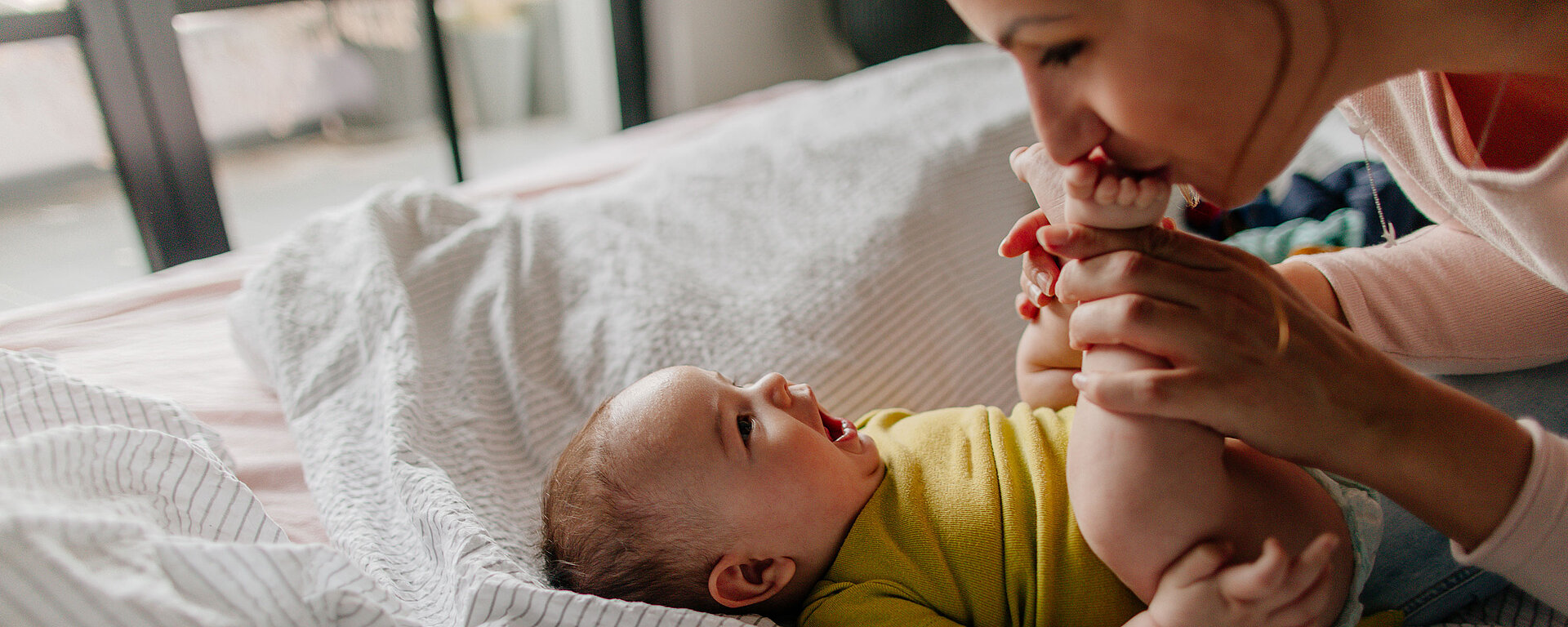 Mother playing with baby on bed, holding baby's feet