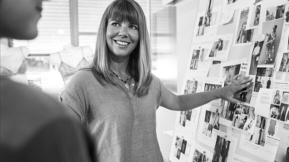 Employee in the mey design department smiling and pointing to a board of design images
